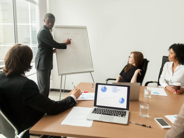 African american businessman giving presentation explains new marketing plan at meeting, black business trainer coach presenting new client management strategy at office training working on flipchart